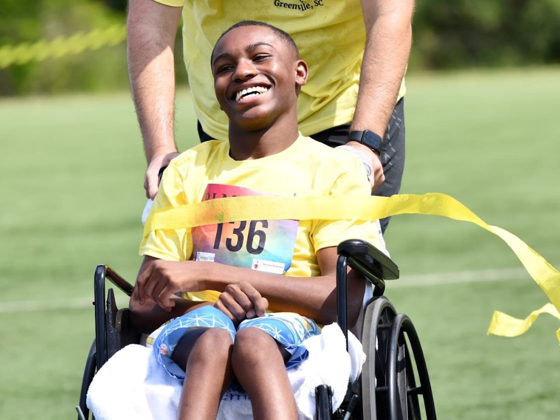 smiling athlete in wheelchair wheeled across finish line