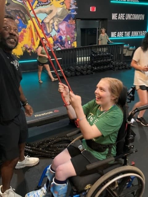 girl in wheelchair works out with stretch band at the Junkyard